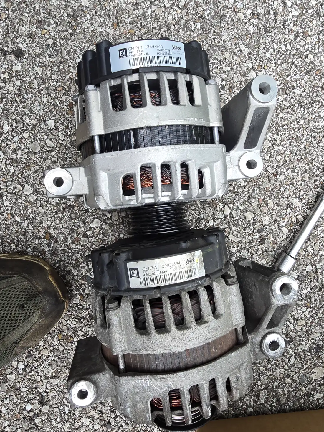 Old and new alternators side by side on the pavement before installation