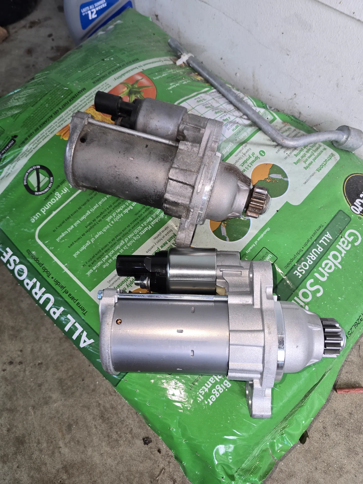 Worn starter motor next to its brand-new replacement, photographed in a customer's driveway